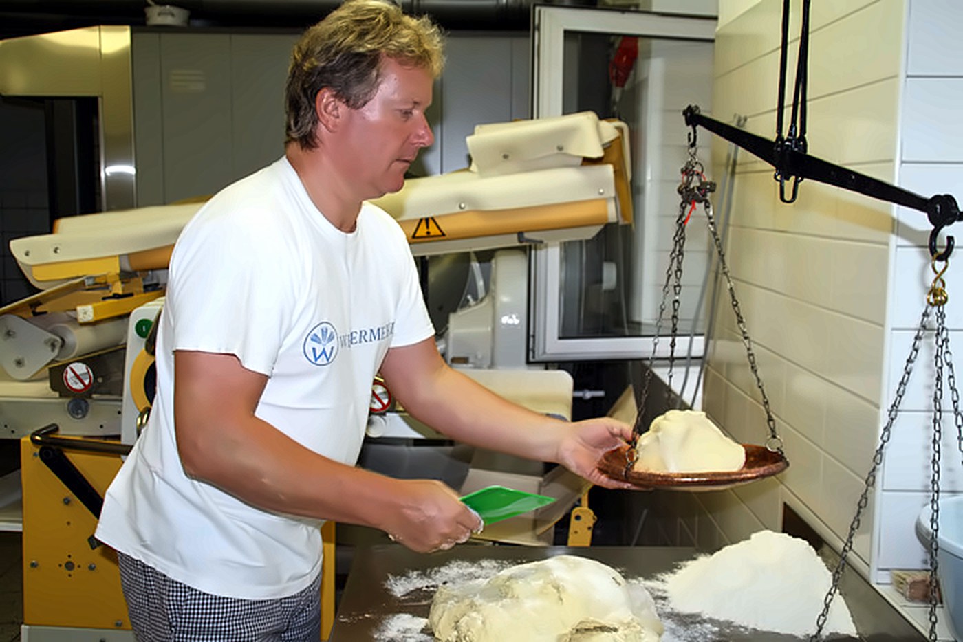 Der Bäckermeister wiegt von Hand Teig auf einer Kettenwaage ab
