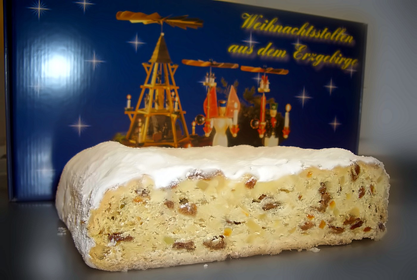 Angeschnittener Erzgebirgischer Weihnachtsstollen mit Puderzucker vor einer Stollenschachtel