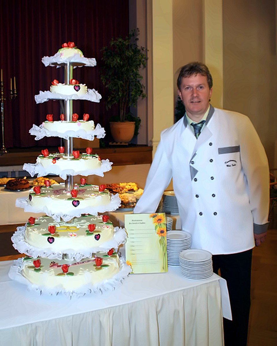 Mehrstöckige Hochzeitstorte mit Marzipanrosen, daneben der Konditor in Berufskleidung